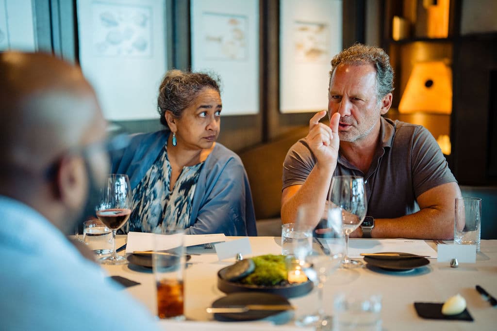 Jonathan Raymond making a point at the set dinner table while a guest listens